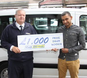 Two men stand in front of a taxi holding a sign that reads £1,000 Prize Draw Winner Cab Direct. Both are smiling and posing, celebrating their prize draw win.
