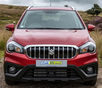 Front view of a red Suzuki SX4 S-Cross SUV taxi parked outdoors on a cloudy day, highlighting the grille, headlamps, and Cab Direct branding on the front number plate. Grass and hills visible in the background.