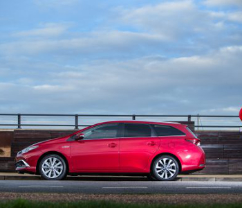 Red Hybrid Special estate car, ideal for taxi services, parked roadside in front of a wooden fence under a partly cloudy sky.