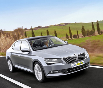 A silver Skoda Superb saloon taxi drives on a rural road with green fields and cypress trees in the background under a blue sky.