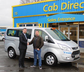 Two men shake hands in front of a silver Ford ProCab™ taxi outside a building labelled Cab Direct Sales Entrance. Both are smiling at what is clearly a car dealership.