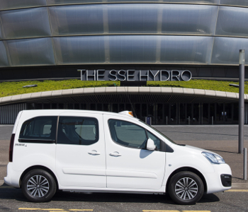 A white Peugeot taxi, part of the Peugeot Premier™ Offer, is parked in front of the SSE Hydro arena with its modern curved façade and large glass panels.
