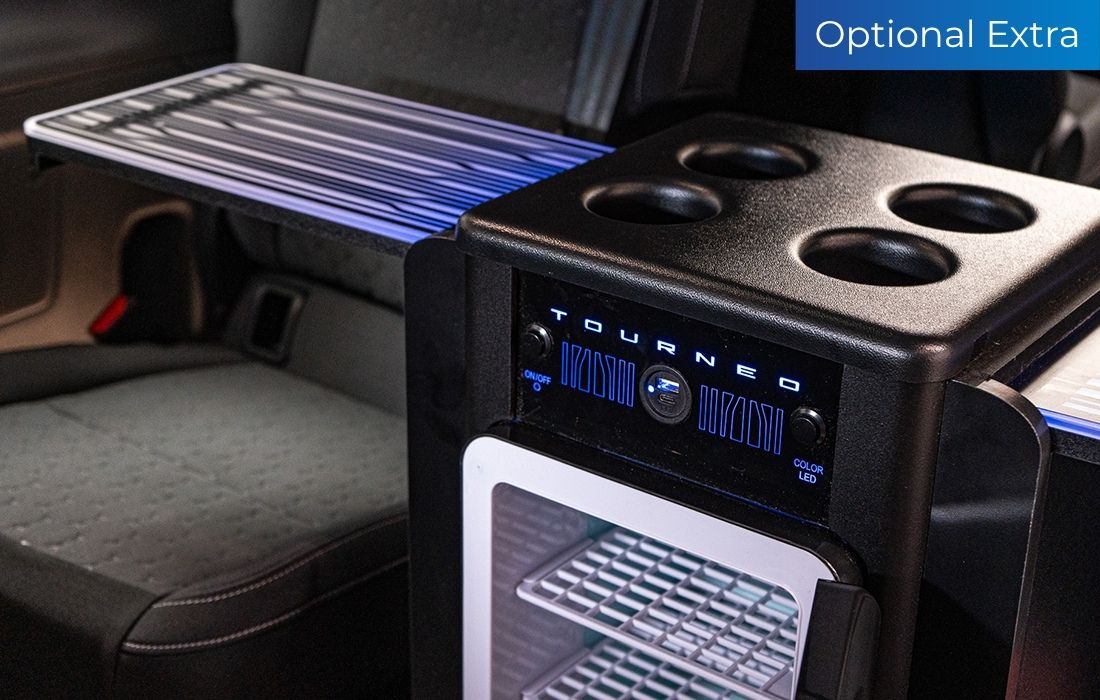 A mini fridge with integrated cup holders and tabletop surfaces is fitted between the seats in the Ford Tourneo Custom Taxi. A blue “Optional Extra” label is visible in the corner.