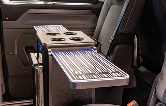 Close-up of the Ford Tourneo Custom Taxi’s backseat area, highlighting the extended tray table with integrated cup holders and a ribbed surface for enhanced passenger comfort and practicality.