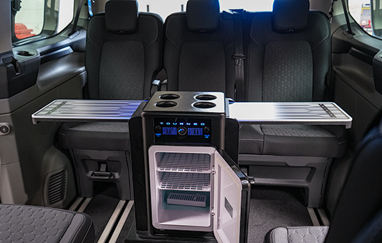 Ford Tourneo Custom Taxi interior with three rear passenger seats, centre console featuring cup holders, fold-out trays, and an illuminated mini fridge with blue LED lighting and empty shelves.