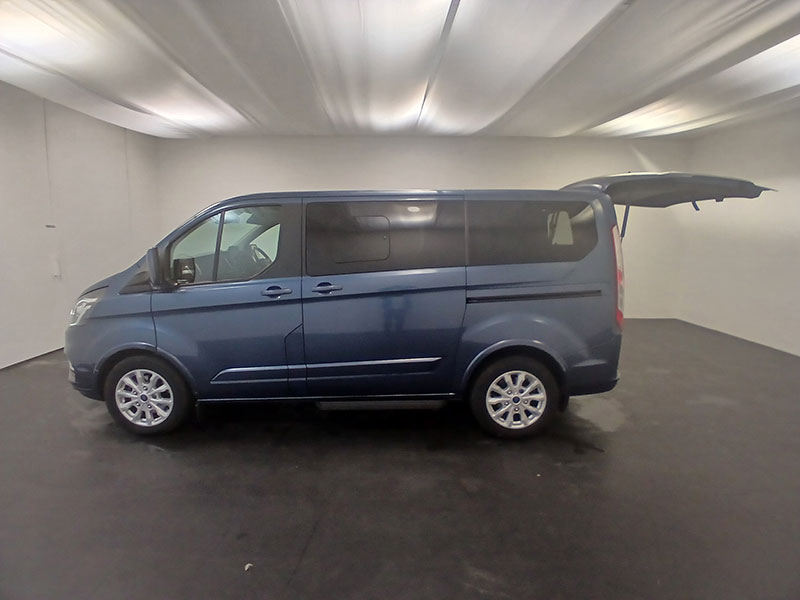 A blue taxi is parked in a spacious, pristine white room with the rear hatch open. Shown from the side, the area surrounding the taxi is clean and minimal, highlighting its condition for sale.