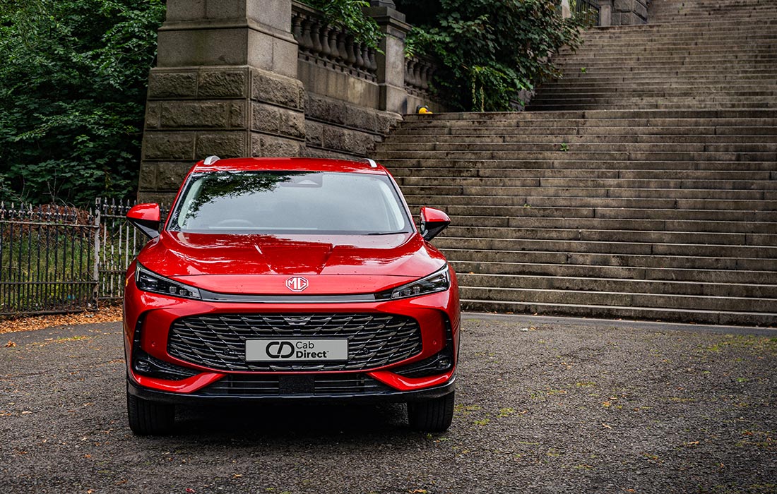 A red MG SUV taxi is parked in front of wide stone steps and a stone wall, with greenery on both sides. The taxi faces forward, highlighting the Cab Direct plate and bold grille design.