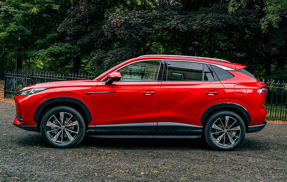 Red SUV taxi parked on gravel, with trees and a black metal fence in the background.