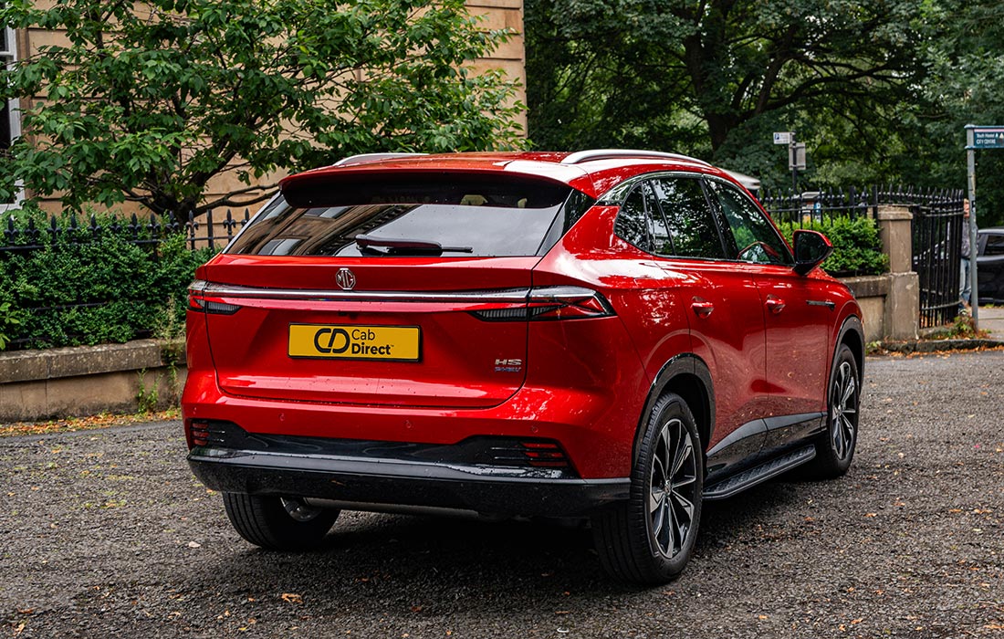 A red SUV taxi with a Cab Direct number plate parked on a gravel surface near greenery and a stone building.