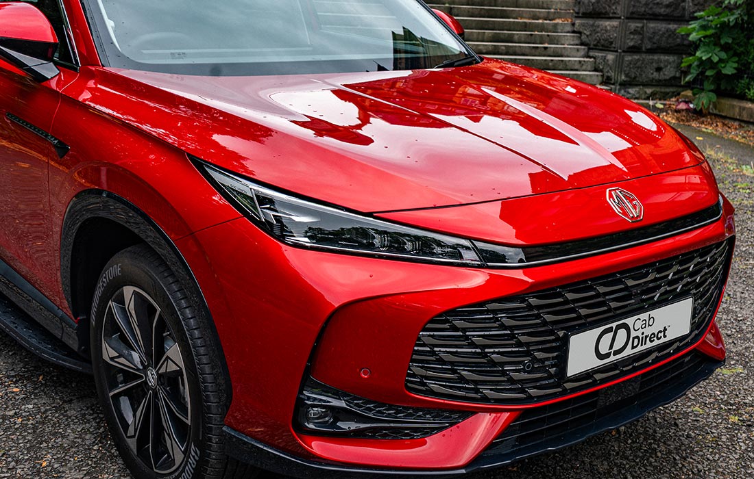 A shiny red MG car with sleek headlamps and a large black grille, parked on a paved surface near stone steps, featuring a front number plate that reads Cab Direct—ideal for taxi services.