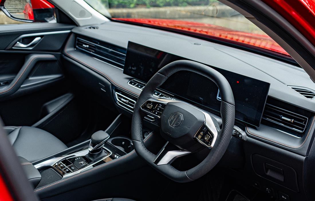 Modern MG car interior featuring a sleek black dashboard, large touchscreen display, and a leather-wrapped steering wheel with the MG logo; red exterior visible on the door frame—ideal for taxi use.