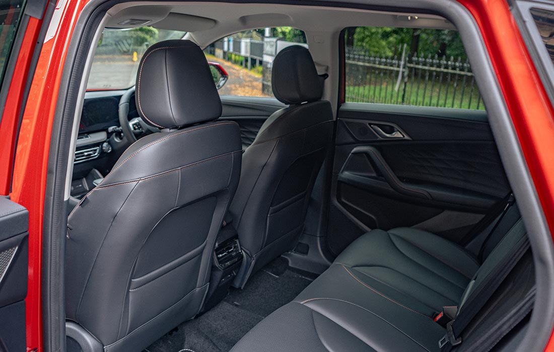 Rear view of a taxi’s black leather interior, featuring spacious back seats, comfortable front seats, and part of the dashboard, with the rear passenger door open and green trees visible outside.