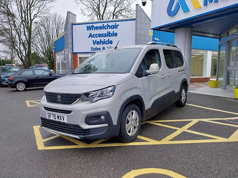 A white Peugeot car is parked in a yellow-striped accessible parking bay outside a building with a sign reading Wheelchair Accessible Vehicle Sales & Service, ideal for taxi use.