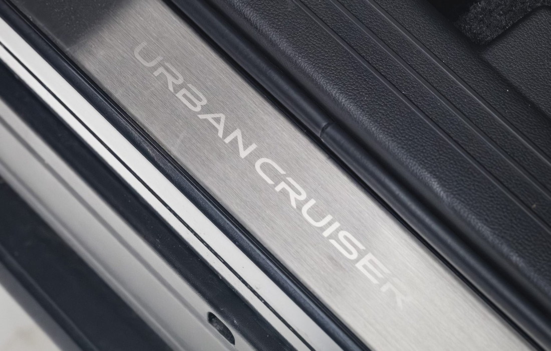 Close-up of a metallic car door sill plate with Urban Cruiser engraved on it, surrounded by black interior trim, highlighting the stylish entryway of this taxi.