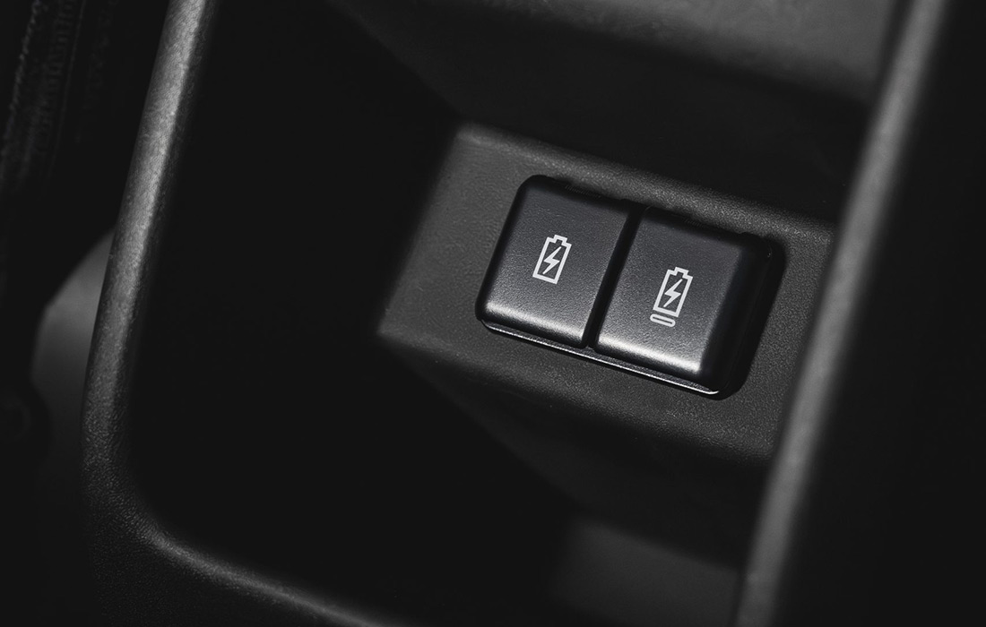 Close-up of two black buttons with white battery symbols on a dark panel, each displaying unique battery icons indicating control over electrical or charging functions in a taxi.