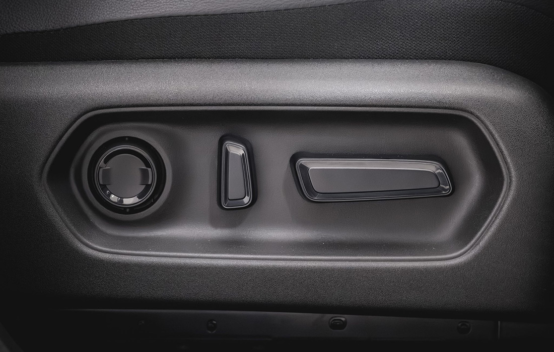 Close-up of black taxi seat adjustment controls, featuring a round knob, a small vertical lever, and a horizontal switch set in a dark plastic panel.
