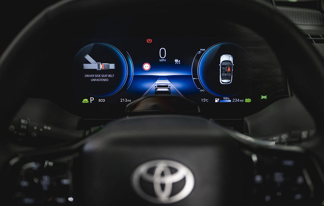 Digital dashboard of a Toyota car showing speed, driving lane, gear, fuel level, temperature, and driver seat belt warning. Toyota-branded steering wheel visible in the foreground; ideal features for a modern taxi.