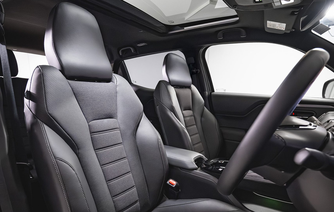 Premium black leather interior of a modern taxi, featuring comfortable driver and front passenger seats, sleek steering wheel, centre console, and sunroof illuminated by natural light.