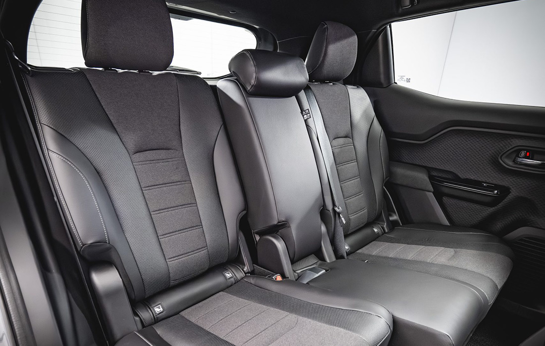 Black leather rear taxi seats with headrests, seat belts, and detailed stitching, viewed from the passenger side under natural lighting in a modern interior.
