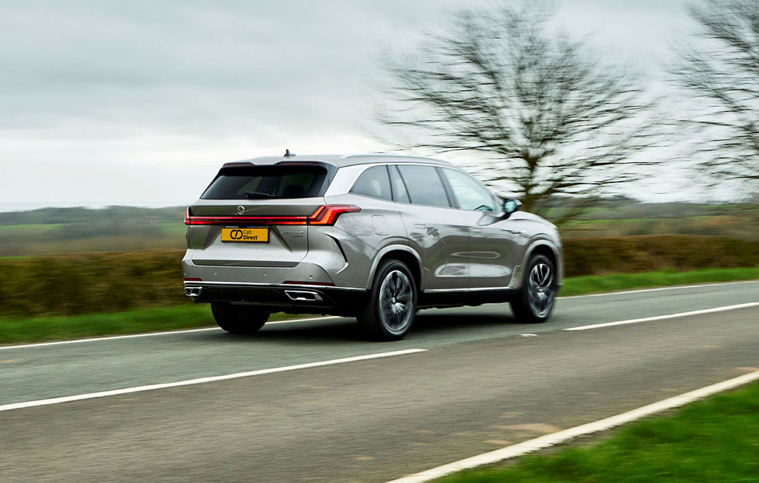 A silver SUV taxi drives on a rural road with blurred trees and fields in the background, highlighting its reliable performance even on cloudy days.