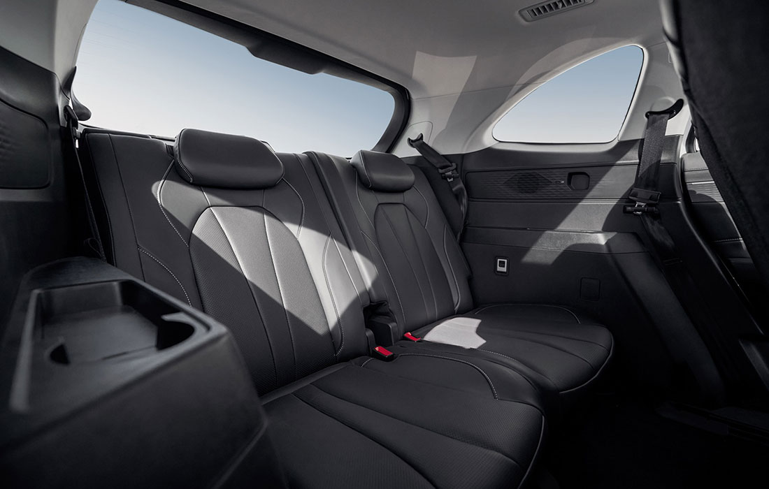 Back seat view of a modern taxi interior featuring black leather seats, three adjustable headrests, seat belts, spacious legroom, and sunlight streaming through large side windows.