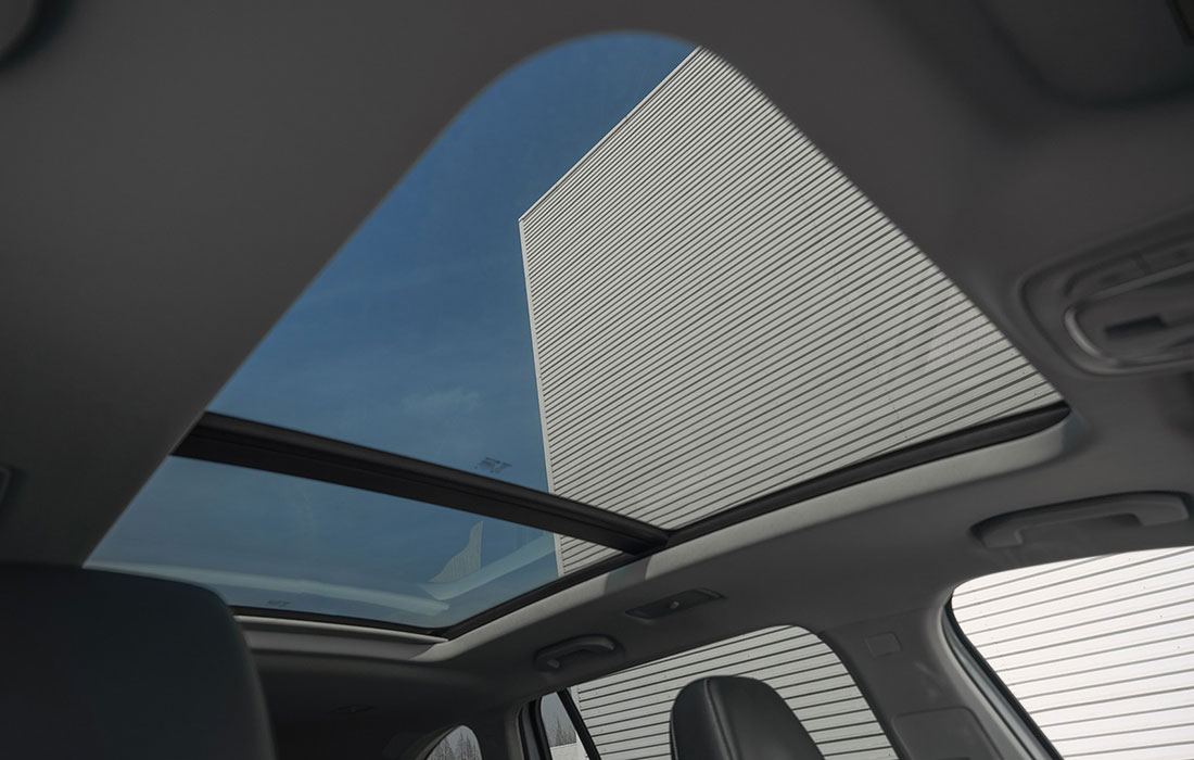 Panoramic sunroof view from inside a taxi, showcasing interior features, blue sky, and a modern building with horizontal cladding—ideal for commercial taxi buyers.