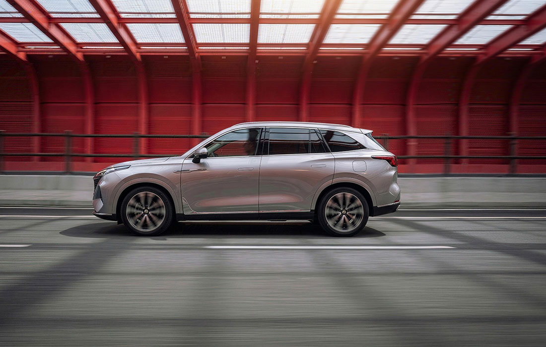 A silver SUV taxi driving on a road beneath a red bridge structure, blurred background emphasising speed.