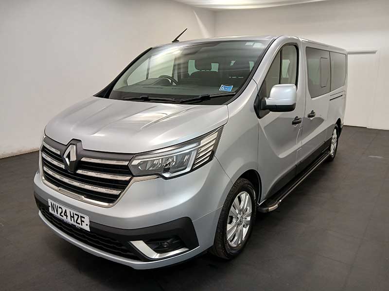 A silver Renault taxi is parked indoors on a dark floor, facing left. Featuring a UK number plate NV24 HZF and side windows, this vehicle displays a clean, modern design ideal for taxi services.