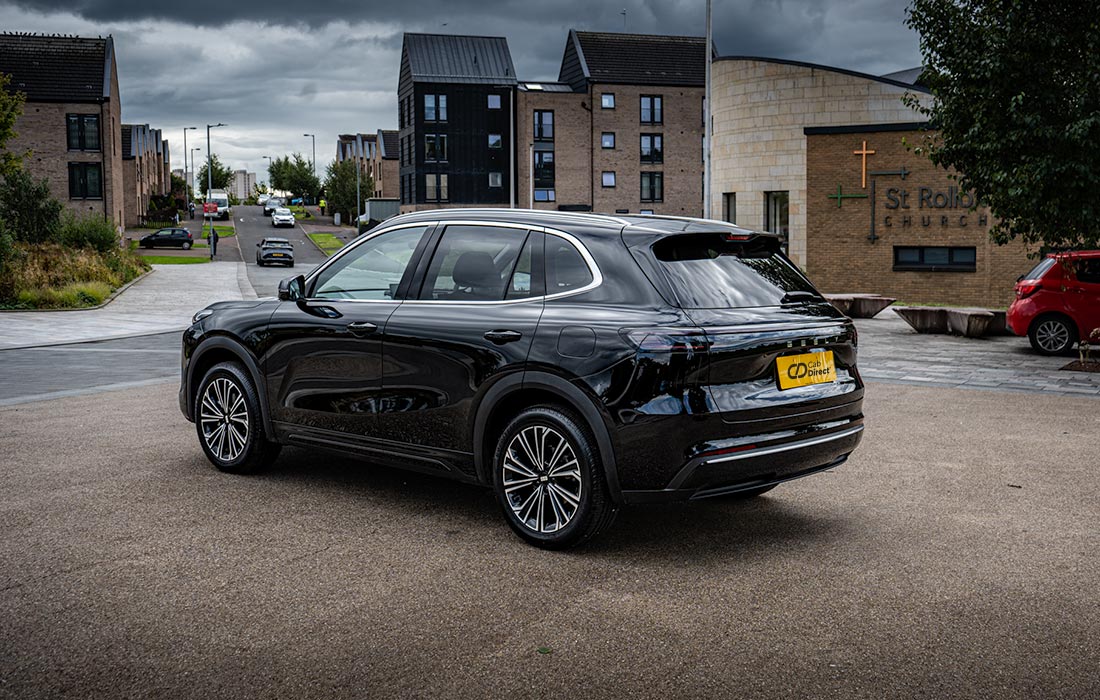 A black SUV taxi is parked on a paved car park near modern buildings and a church, under overcast skies.