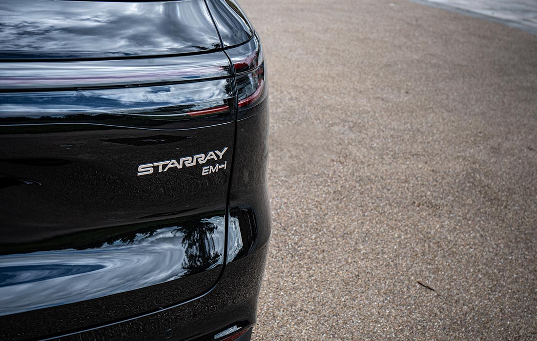 Close-up of the rear side of a black car, ideal for commercial use, parked on gravel with a visible STARRAY EM-H badge and part of the tail light.