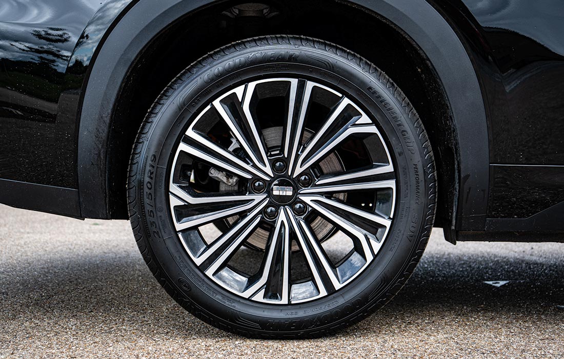 Close-up of a taxi’s alloy wheel featuring a sleek black and silver multi-spoke design, fitted with a black tyre, shown on a paved surface beside the taxi’s glossy black body.