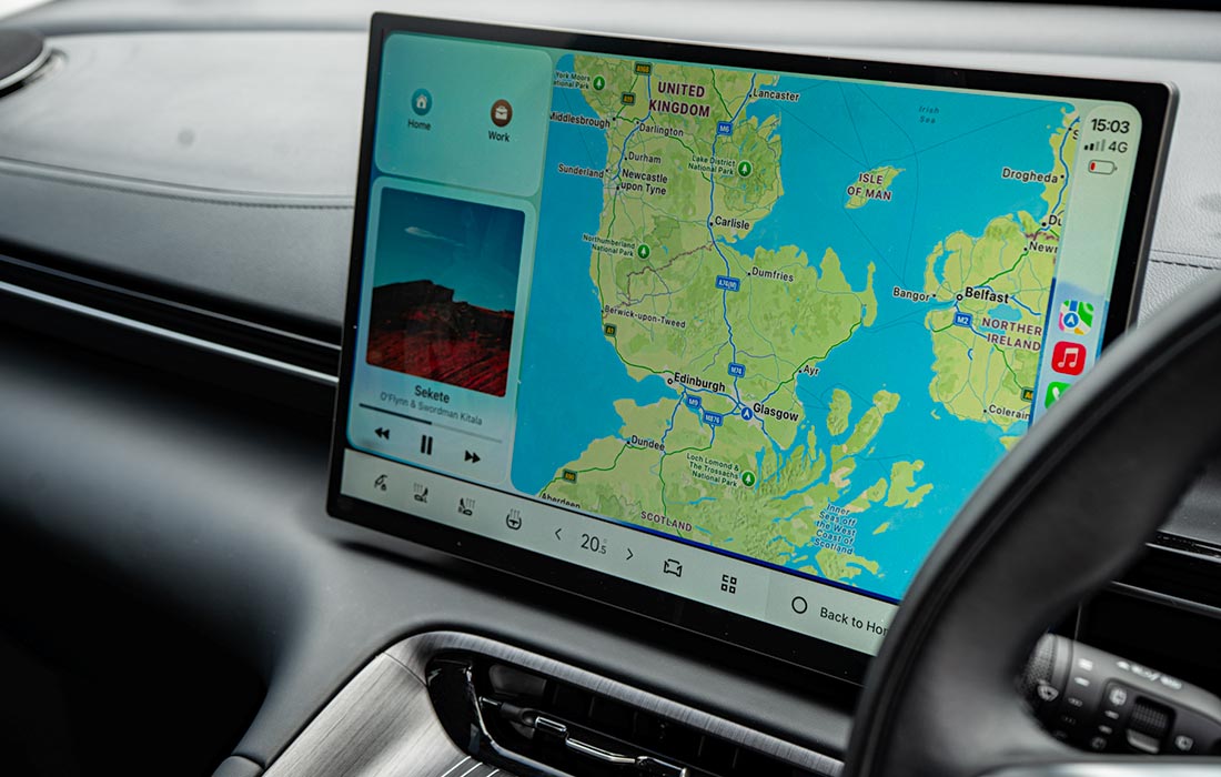 A taxi’s dashboard screen shows a navigation map of the United Kingdom, music controls on the left, and app icons on the right.