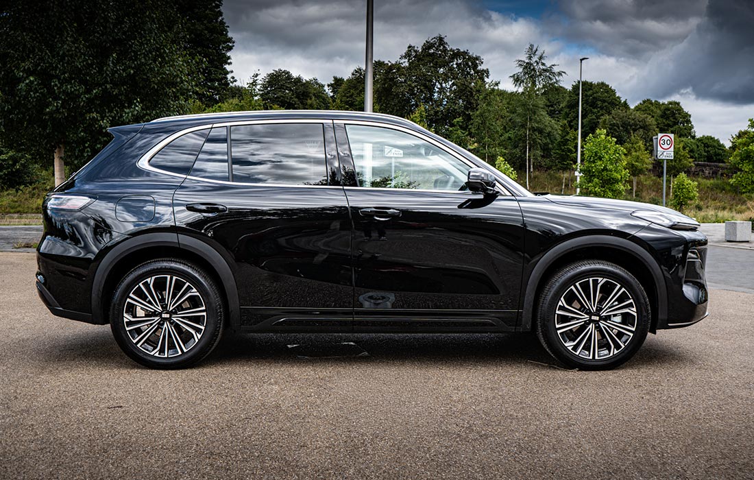 A shiny black SUV taxi parked on a paved surface, with trees and a cloudy sky in the background. Side view highlights its modern design and alloy wheels—ideal for commercial taxi services.