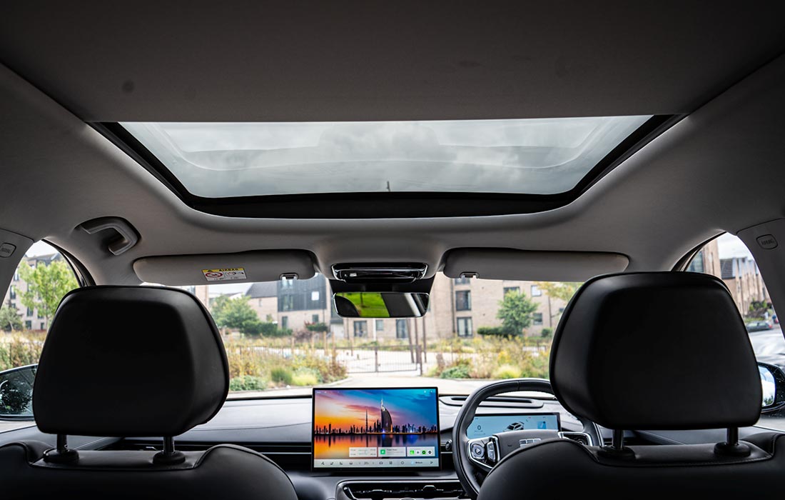 Interior view of a modern taxi showcasing a spacious sunroof, comfortable front seats, digital dashboard, and wide touchscreen display, with street and buildings visible through the windows.