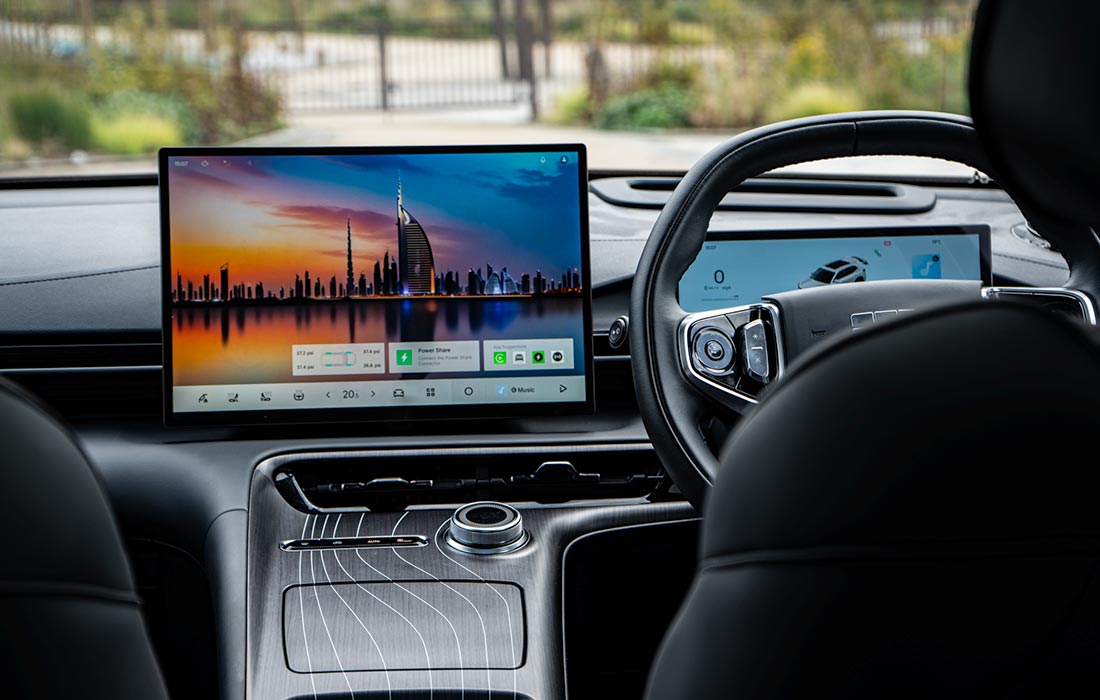Modern taxi interior featuring a digital dashboard and large central touchscreen displaying a city skyline at sunset, with visible steering wheel and centre console.