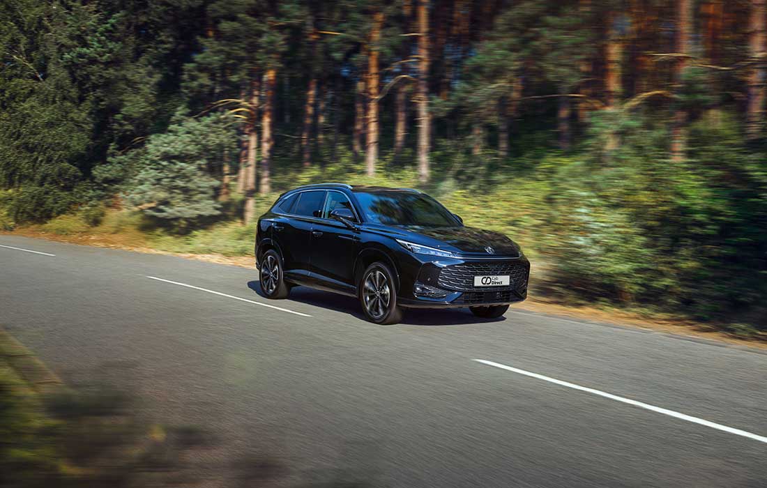 Black LEVC taxi driving on a road lined with pine trees.