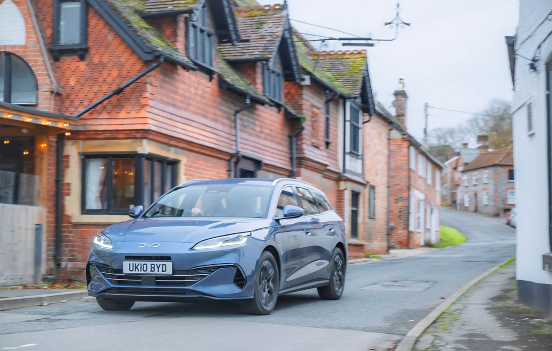 Blue BYD Dolphin taxi driving on a street lined with historic brick buildings.