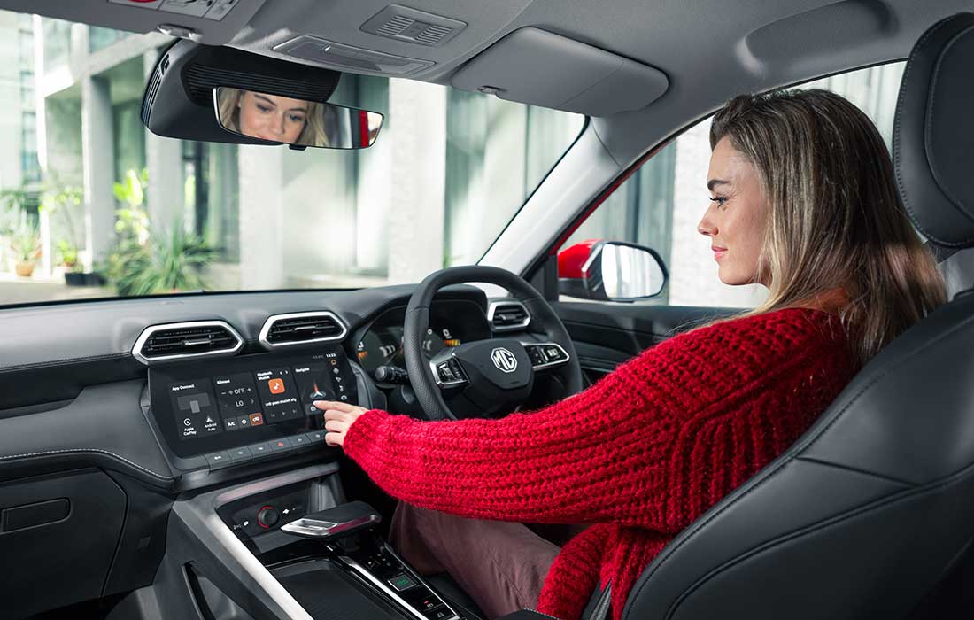 A woman in a red jumper sits in the driver’s seat of an MG taxi, interacting with the touchscreen infotainment display.