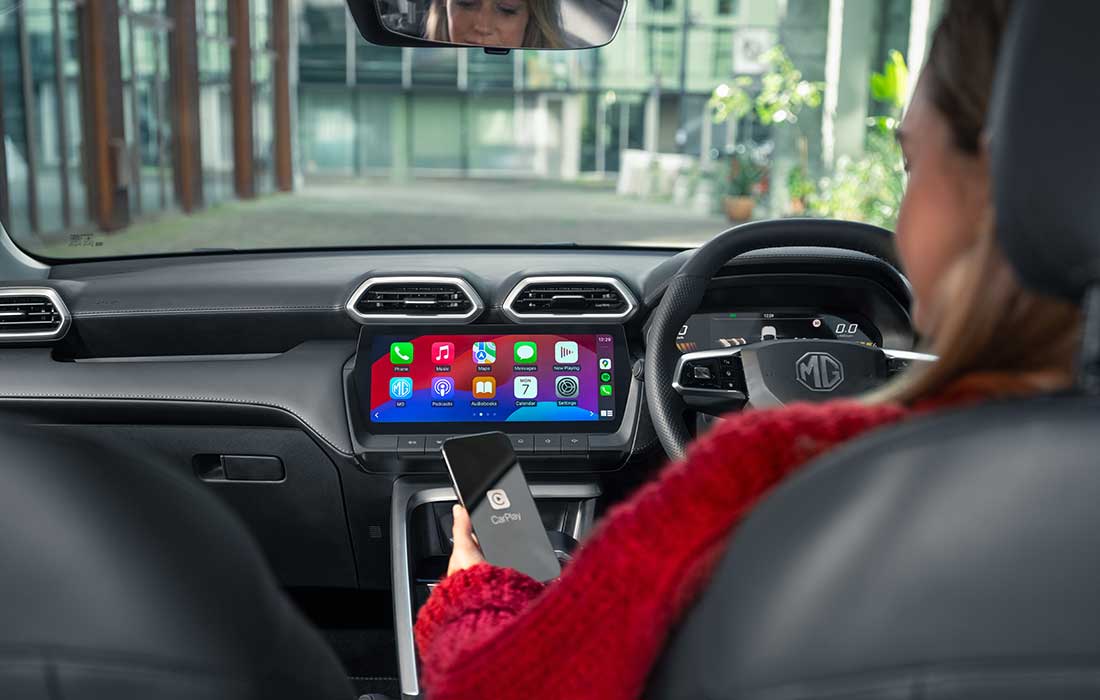 Driver in an MG taxi connecting a smartphone to the Apple CarPlay infotainment display.