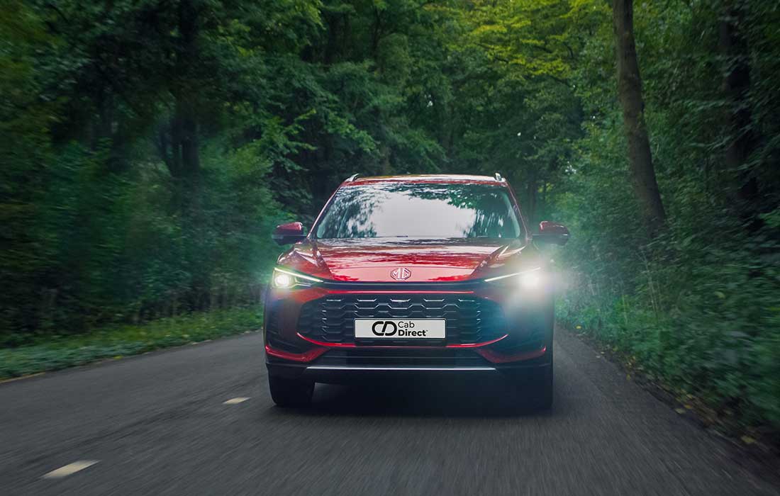Red MG taxi driving along a road through a forest.