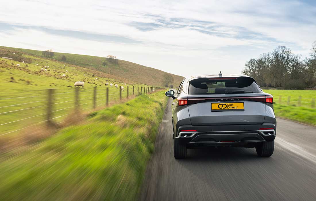 Grey taxi driving along a rural road next to a grassy hill with sheep.