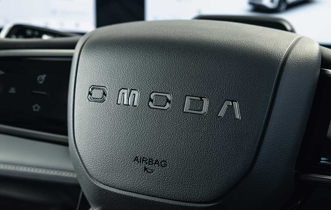 Close-up of an OMODA taxi steering wheel centre with the brand name embossed in silver lettering.
